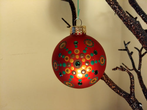 A painted starburst design in gold and green on a red ornament. Embellished with crystals.