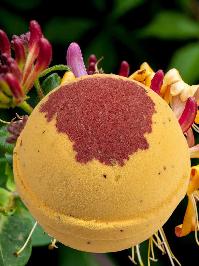 Yellow bath bomb with red design on top.