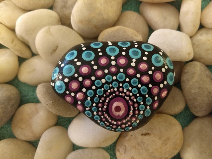 A small stone with a triangular design in lilac and teal on a black background.