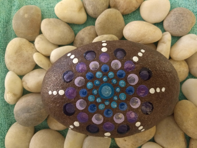 Large hand size stone with a starburst design in teal and purple on a natural background. 