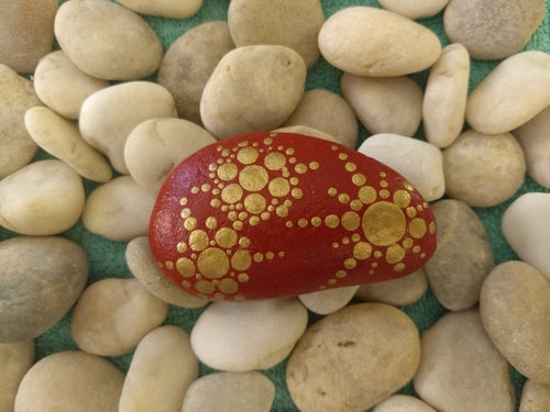 A small stone with a gold snowflake design on a red background.