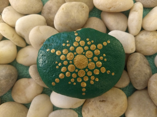 A small stone with a gold snowflake design on a green background.