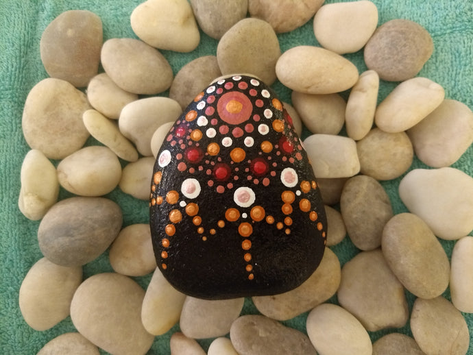 A hand-sized stone with a painted starburst pattern in red and orange.