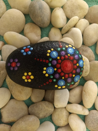 A palm-sized stone with a painted rainbow starburst design on a black background.