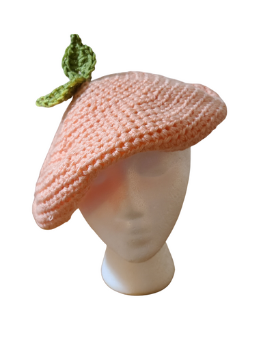 Crocheted yarn hat. Peach colored yarn. Green crocheted leaf on top