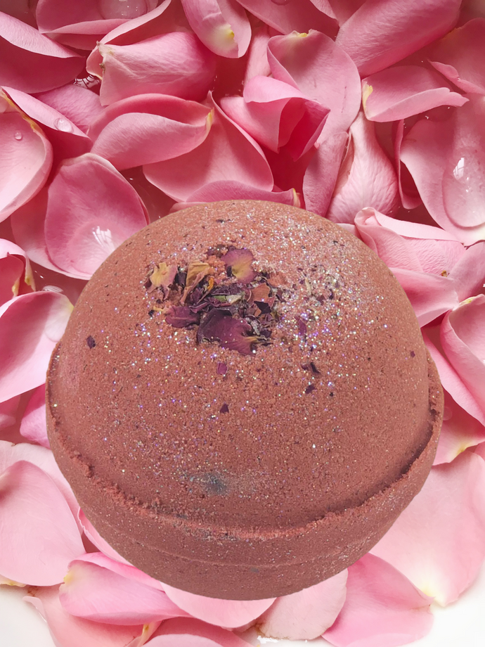 Rose colored bath bomb with decorative petals on top.