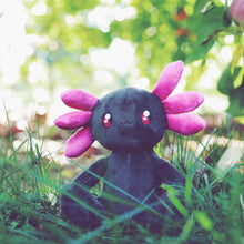 Load image into Gallery viewer, A smiling anthropomorphic black axolotl sits. It&#39;s body is black, while it&#39;s external frilly gills are a darker pink, and it has red eyes. 
