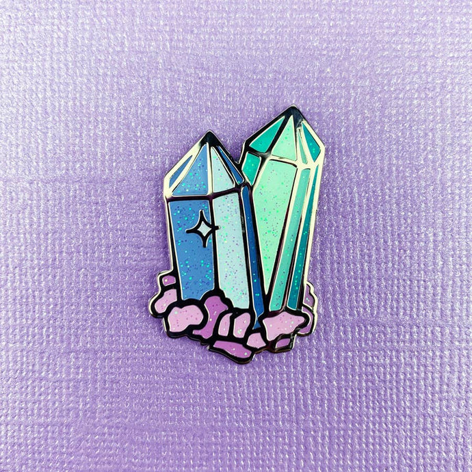 Enamel pin depicting two sparkling, stylized celestite crystals.