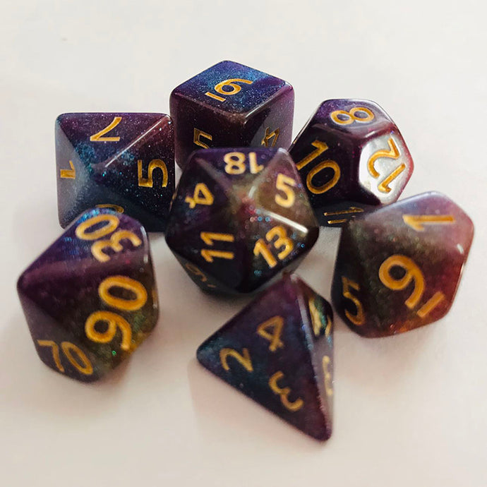 A tabletop dice set in a gradient tone including sparkling black, deep blue, gold, and purple, with gold numbers.