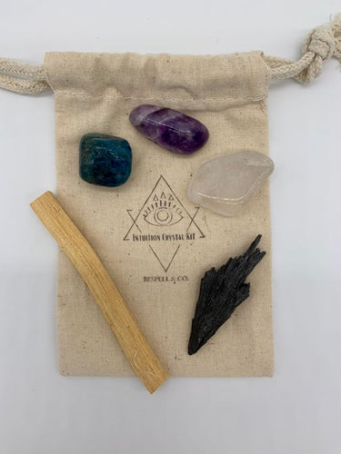 A cotton bag containing a black kyanite, a quartz crystal, an amethyst crystal, an apatite crystal, a palo santo stick, and a brass third-eye charm