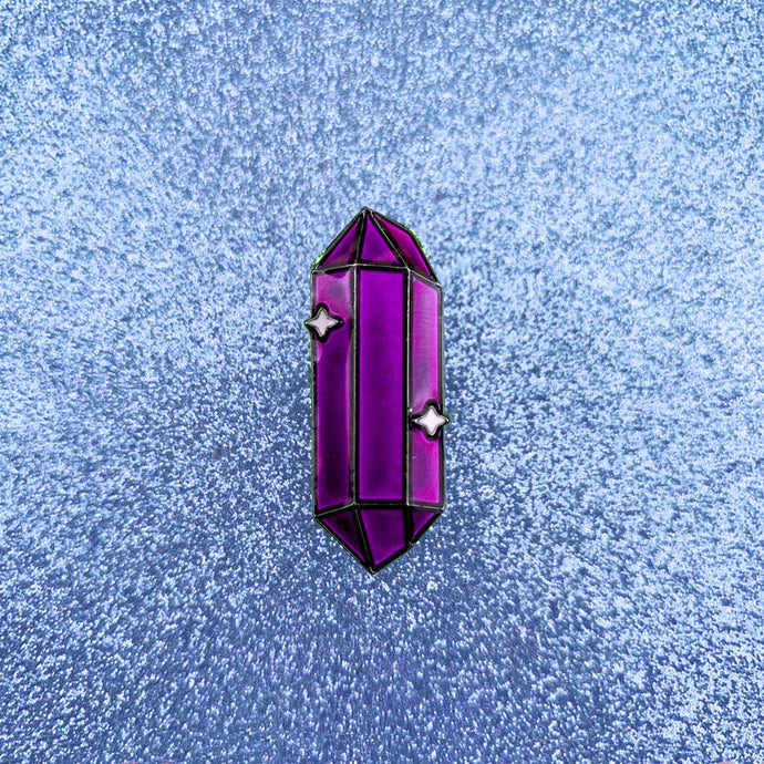 Enamel pin depicting a sparkling, stylized deep purple crystal.