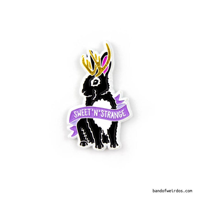Enamel pin depicting a black-and-white jackelope with golden horns and a purple ribbon that says 