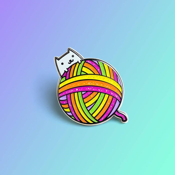 Enamel pin depicting a smiling white cat with a giant ball of colorful yarn.